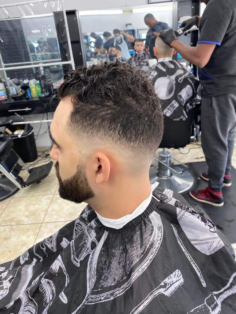 Curly top fade with a full beard, shop floor in the background