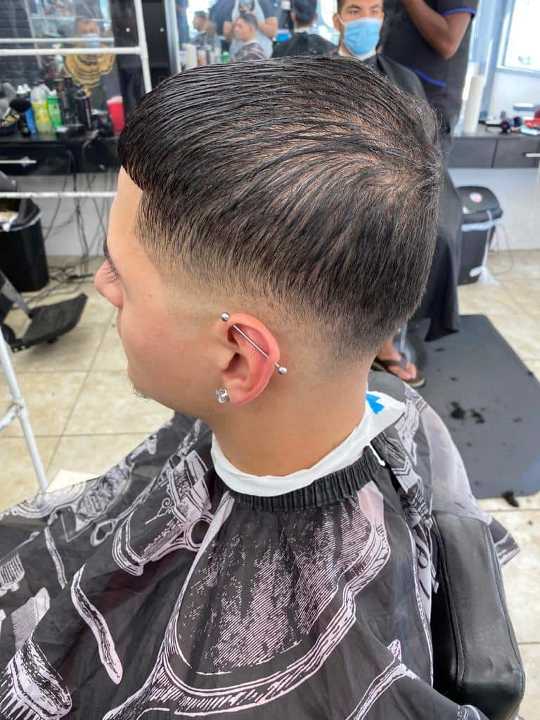 Slicked-back taper with a sharp part and ear piercing detail